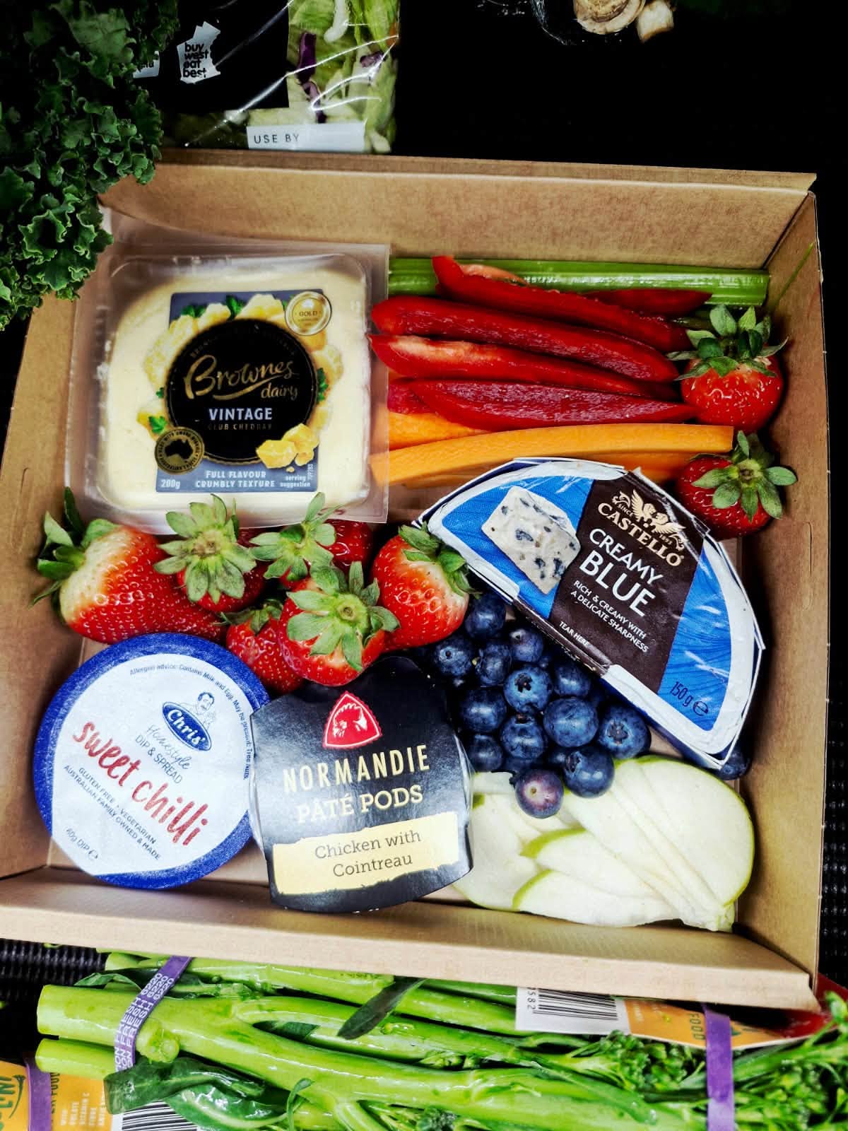 Fresh strawberries, blueberries, apple slices and vegetable sticks in a cardboard box